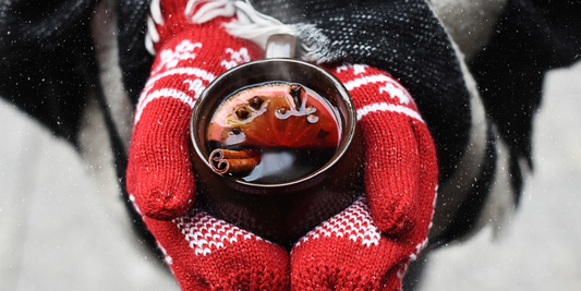 Tasse mit Glühwein wird mit Handschuhen festgehalten