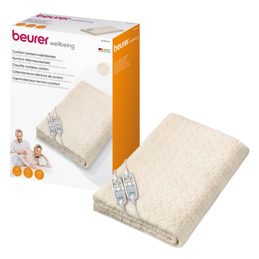 Ein Beurer Komfort-Wärmeunterbett UB 86 Teddy Double wird neben seiner Verpackung ausgestellt. Auf der Verpackung sind ein Familienbild, der Markenname Beurer GmbH, Produktdetails und ein Bild der Decke mit ihrer Steuerung zu sehen. Das beige Wärmeunterbett verfügt über eine weich strukturierte Oberfläche, die perfekt für gemütliche Nächte ist.