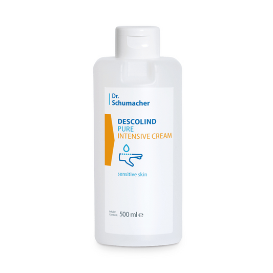 Eine 500-ml-Flasche Dr. Schumacher Descolind Pure Intensiv-Pflegecreme von Dr. Schumacher GmbH wird ausgestellt. Die Flasche hat ein weißes Etikett mit blauem und orangefarbenem Text, der angibt, dass sie ideal für „empfindliche und trockene Haut“ ist. Das Etikett zeigt außerdem eine minimalistische Grafik einer Hand, die die parfümfreie Intensiv-Pflegecreme aufträgt.