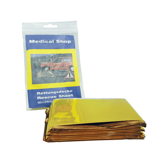 Davor liegt eine gefaltete, gelbgoldene Rettungsdecke aus aluminiumbeschichteter Polyesterfolie. Dahinter befindet sich ein Paket mit der Aufschrift „Holthaus Medical Rettungsdecke, gold silber“ der Holthaus Medical GmbH & Co. KG, das eine Unfallszene mit einem roten Auto zeigt und die Maße 160x210 cm aufweist.