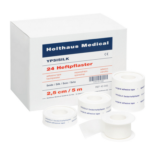 Eine Schachtel mit der Aufschrift „Holthaus Medical GmbH & Co. KG“ mit „Holthaus YPSISILK Heftpflaster – 2,5 cm x 5 m | Packung (5 m)“ und mehreren Rollen weißem Klebeband in verschiedenen Größen davor. Der Text auf der Schachtel und den Bändern enthält Produktdetails in mehreren Sprachen.