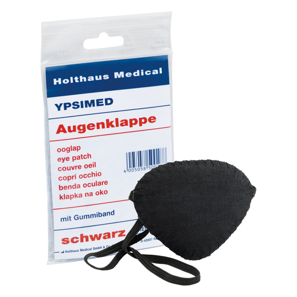 Ausgestellt ist eine Holthaus Ypsimed Augenklappe, mit Gummiband, aus schwarzem Stoff. Daneben befindet sich eine Kunststoffverpackung mit der Aufschrift „Holthaus Medical GmbH & Co. KG“, „YPSIMED“ und „Augenklappe“ in mehreren Sprachen, die auf die Verwendung als medizinisches Hilfsmittel für den Augenschutz hinweist.