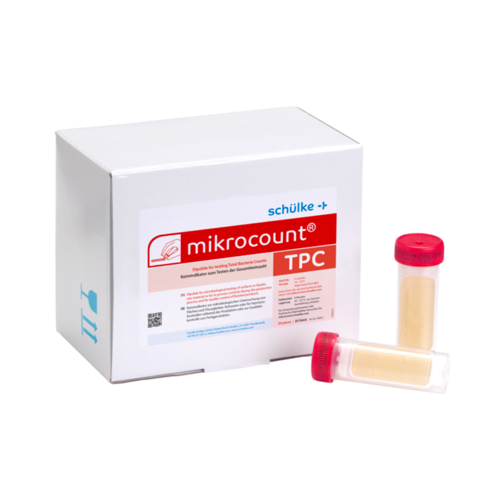 Eine weiße Schachtel mit der Aufschrift „Schülke & Mayr GmbH Mikrocount® TPC, Nährboden | Packung (20 Stück)“ mit einem Logo und einer Produktbeschreibung neben zwei Fläschchen für mikrobielle Tests, eines mit gelbem Deckel, das andere mit durchsichtigem Deckel.