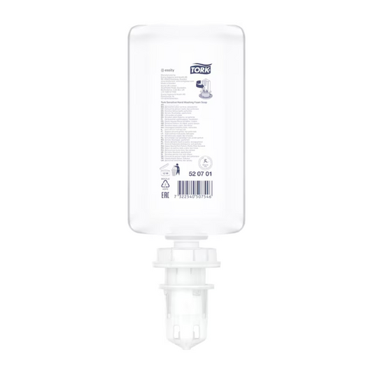 Eine durchsichtige, rechteckige Plastikflasche mit der Aufschrift „Tork 520701 Sensitive Hand-Schaumseife Premium S4 | Karton (6 Flaschen)“ mit Produktdetails und Anleitung in schwarzem und grauem Text. Die Flasche hat unten einen weißen Pumpmechanismus, der auf ihre Verwendung als Spender hinweist, wahrscheinlich für allergikerfreundliche Seife oder Desinfektionsmittel.