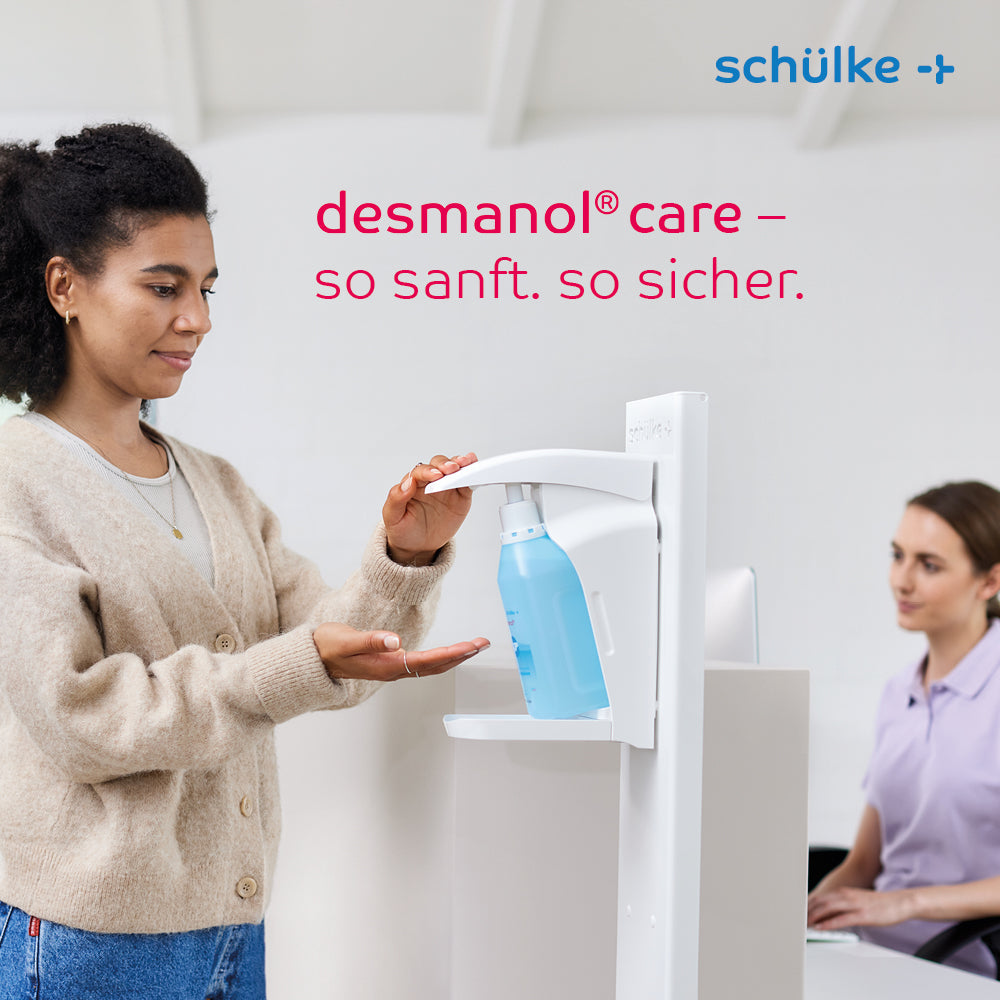 Eine Frau benutzt an einer Theke einen Schülke desmanol® care Händedesinfektionsmittel-Spender, während eine andere Frau in der Nähe sitzt und an einem Computer arbeitet. Der Text „desmanol® care – so sanft. so sicher.“ und die Marke „Schülke & Mayr GmbH“ werden präsentiert, wobei die Hautpflege-Formel für die sanfte und wirksame Anwendung von Händedesinfektionsmittel im Vordergrund steht.