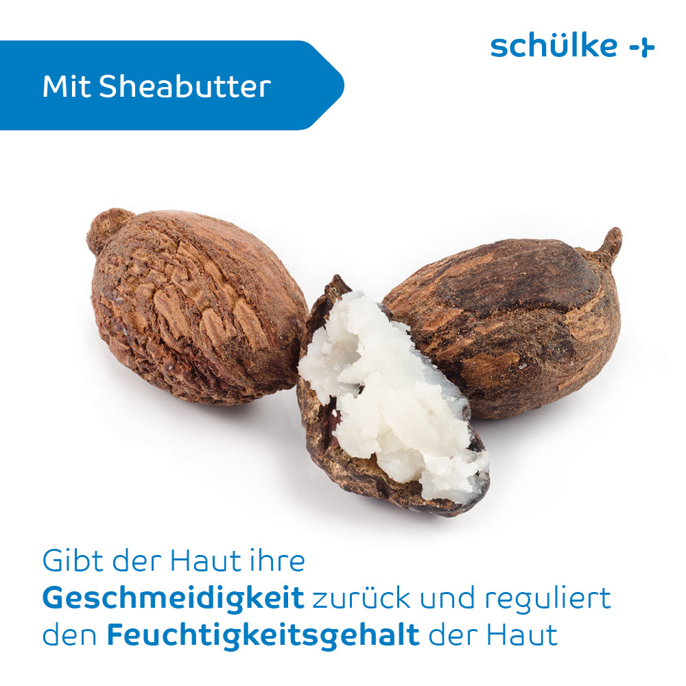 Das Bild zeigt drei Shea-Nüsse, von denen eine aufgeschnitten ist, um die weiße Sheabutter im Inneren freizugeben. Der deutsche Text oben links lautet: „Mit Sheabutter.“ Unten heißt es in der Überschrift: „Gibt der Haut ihre Geschmeidigkeit zurück und reguliert den Feuchtigkeitsgehalt der Haut. Farbstoff- und parfümfrei für intensive Pflege. Schülke sensiva® dry skin Hautbalsam von Schülke & Mayr GmbH.“